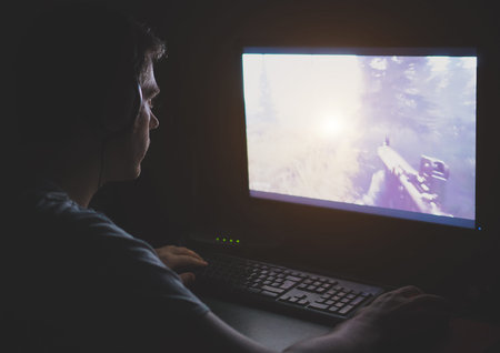 Man in headphones playing computer shooter game at night.