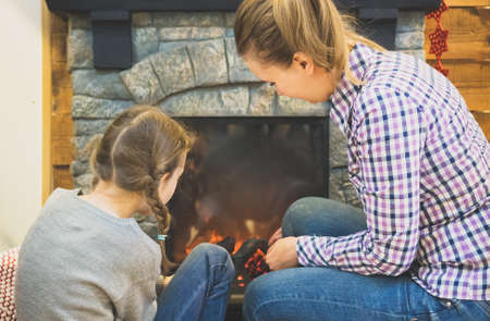 Mom and daughter are sitting near the electronic fireplace.の写真素材