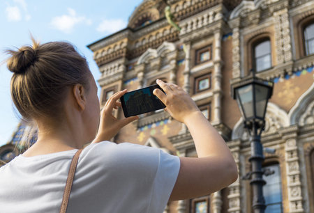 Woman taking pictures of Church of the Savior on Blood with smartphone.
