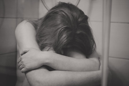 Depressed woman sitting in the shower cabin.