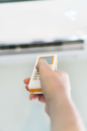 Hand holding remote control aimed at the air conditioner.の写真素材