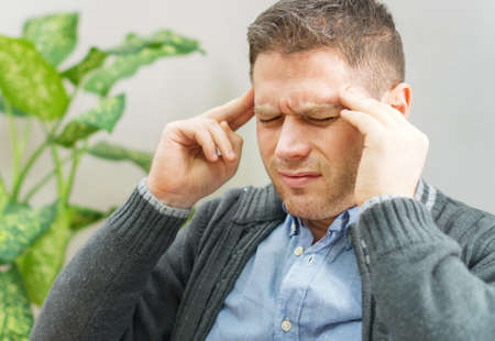 Handsome unshaved man having a headache at home.の写真素材