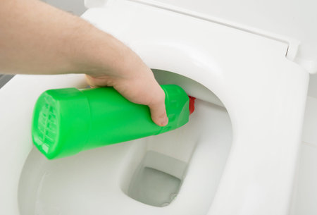 Male hand cleaning toilet bowl at water closet.