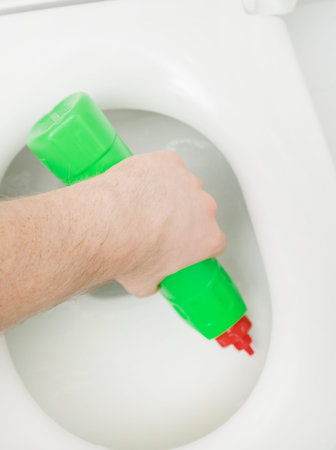Male hand cleaning toilet bowl at water closet.