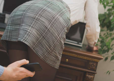Sexual harassment at work. Man taking a photo with mobile phone of secretary's butt.の写真素材