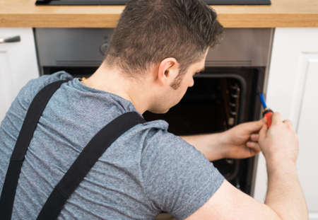 Professional handyman in overalls repairing domestic oven in the kitchen.の写真素材