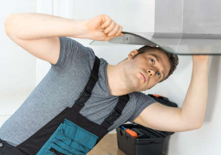 Handsome foreman fixing exhaust hood in the kitchen.の写真素材