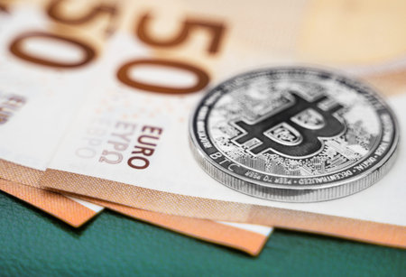 Silver bitcoin coin cryptocurrency lying on the euro banknotes.