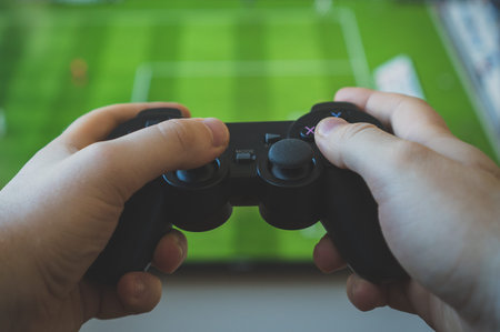 Man playing soccer video game on TV. Gamepad controller in hands.