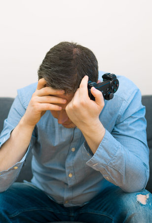 Sad man with gamepad in hands playing video game.
