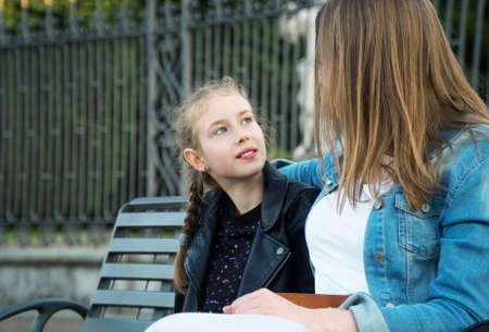 Mom and her daughter are sitting on a park bench and talking.の写真素材