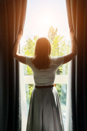 Woman opening curtains in the hotel room at sunny morning.の写真素材