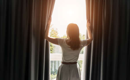 Woman opening curtains in the hotel room at sunny morning.の写真素材
