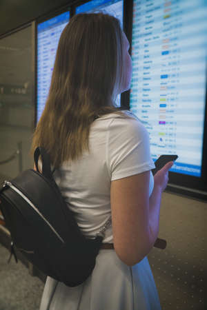 Woman in front of flight information board, checking her flight.の写真素材
