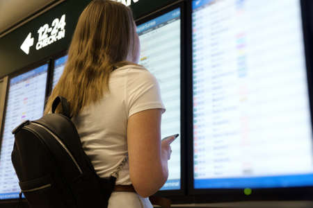Woman in front of flight information board, checking her flight.の写真素材