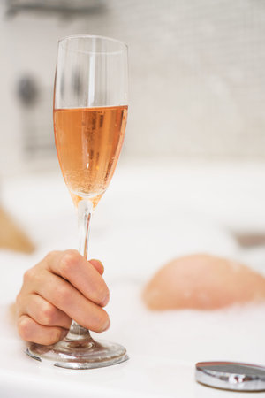 Woman with glass of wine is relaxing in bathtub.
