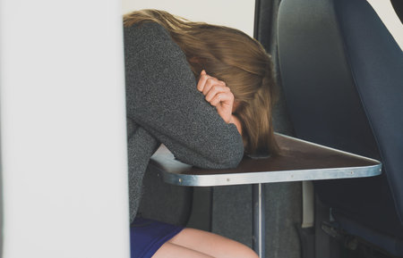 Female criminal sitting in police van and covers her face with her hand.