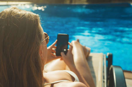 Pretty lady in sunglasses using smartphone near the pool in the summer.の写真素材