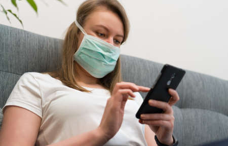 Woman in medical mask using mobile phone. Isolation at home.の写真素材