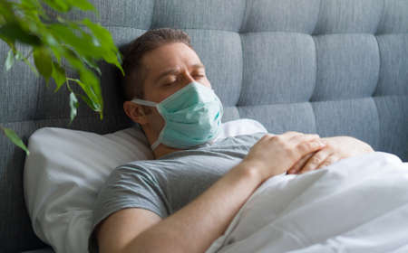 Sick man with medical mask lying in bed.の写真素材