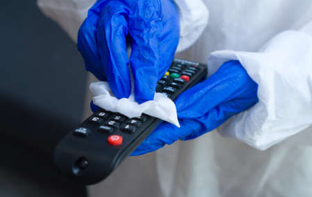 Hand in protective glove with napkin cleaning remote control. Covid-19 disinfection concept.の写真素材