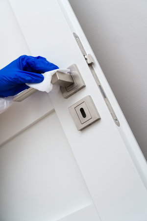 Hand in protective glove with napkin cleaning door handle. Covid-19 disinfection concept.