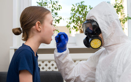Male doctor in protective suit and mask taking swab sample from child.