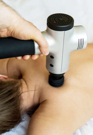 Man massaging woman's back with massaging percussion device. Percussion therapy.の写真素材