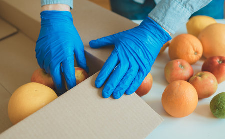 Volunteer in protective medical gloves putting fruits In donation box.