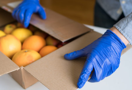 Volunteer in protective medical gloves putting fruits In donation box.