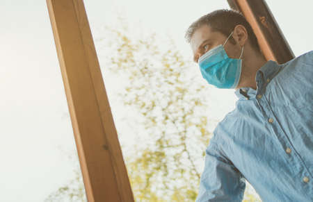 Man in medical mask stands on the balcony and breathes fresh air. Stay home.の写真素材