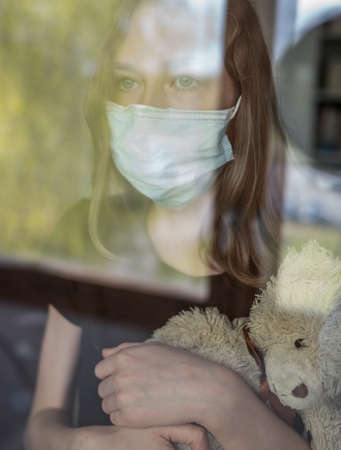 Little girl with toy behind the window during self isolation. Stay home.の写真素材