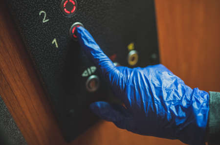 Hand in glove pressing the elevator button.の写真素材