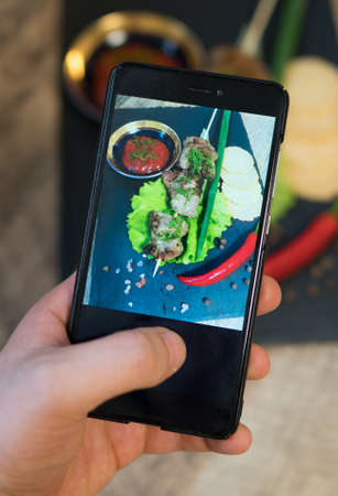 Woman doing photo of shashlik on mobile phone.の写真素材
