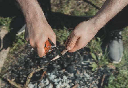 Man with knife cutting wooden stick over bonfire.の写真素材