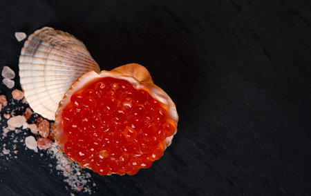 Red caviar in seashell on granite surface. Top view.