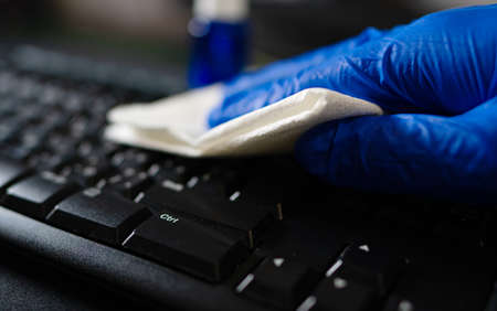 Hand in protective glove with napkin cleaning keyboard. Covid-19 disinfection concept.の写真素材