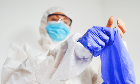 Medical worker in protective suit puts on gloves.の写真素材