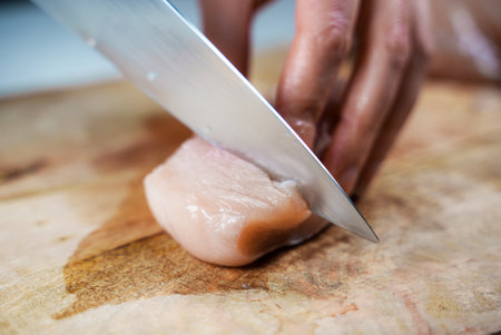Woman is cutting chicken fillet with a knife.の写真素材