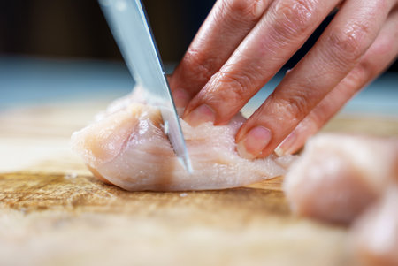 Woman is cutting chicken fillet with a knife.の写真素材