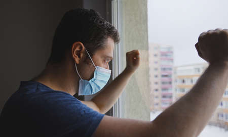 Tired man in medical mask looks out the window.の写真素材