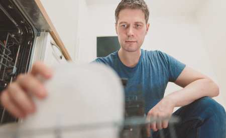Man puts plate to the dishwasher in the kitchen.の写真素材