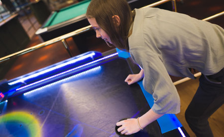 Tween girl plays air hockey in the entertainment center.