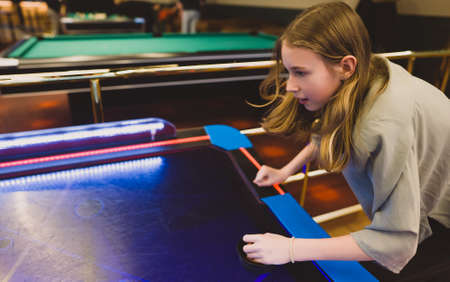 Tween girl plays air hockey in the entertainment center.の写真素材