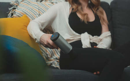 Woman massaging leg with massage percussion device at home.の写真素材