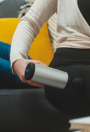 Woman massaging leg with massage percussion device at home.