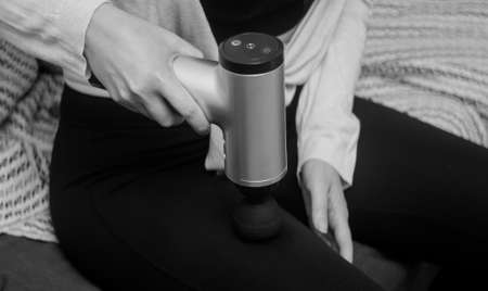 Woman massaging leg with massage percussion device at home.の写真素材