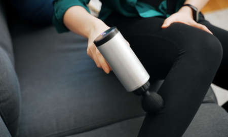 Woman massaging leg with massage percussion device at home.の写真素材