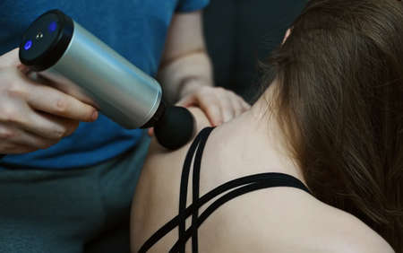 Man massaging woman with massage percussion device at home.の写真素材