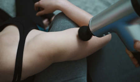 Man massaging woman with massage percussion device at home.の写真素材